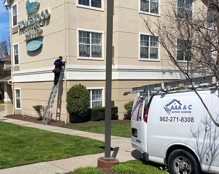 Technician on a ladder at a Homewood Suites job, with the AAA & C van parked beside the building