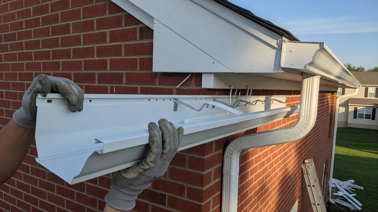 Gloved hands fitting a white gutter on a brick house